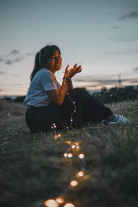 Full length of woman sitting on field against sky during sunset