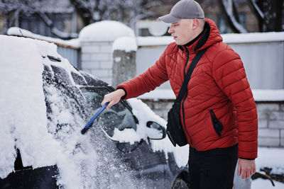 Man cleaning car from snow and ice with brush and scraper tool during snowfall. winter emergency