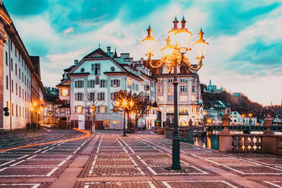 Illuminated street amidst buildings against sky at dusk