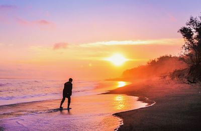 Silhouette man walking at beach against sky during sunset