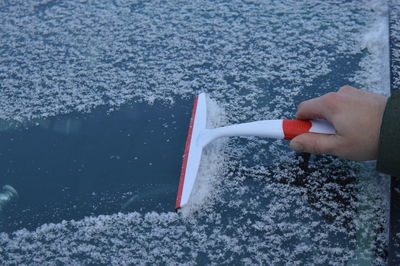 Man cleans car glass from ice. frozen car covered snow at winter day.