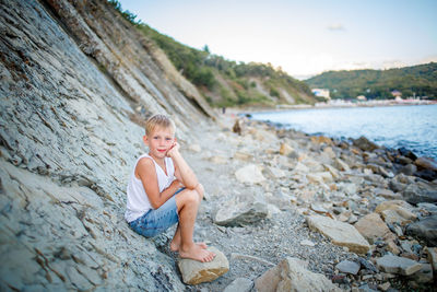 Boy sitting on rock at shore