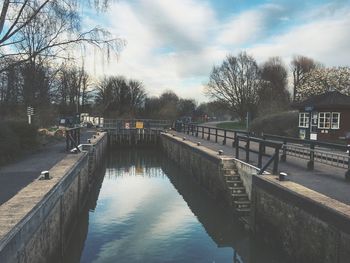 Canal amidst street against cloudy sky