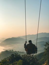 Rear view of men sitting on mountain against sky during sunset