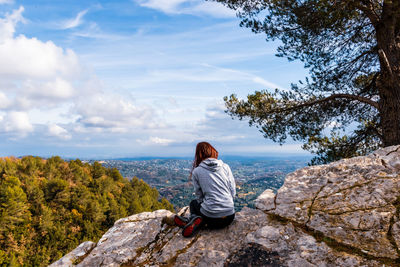 Woman sitting on rock looking at mountain against sky