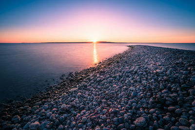 Scenic view of pebbles beach against sky during sunset