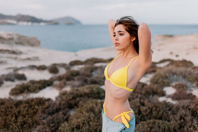 Carefree young woman with hand in hair standing on shore at beach