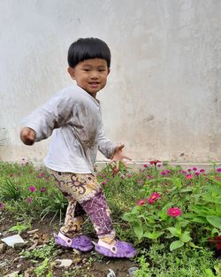 Side view of cute boy standing by flowering plants