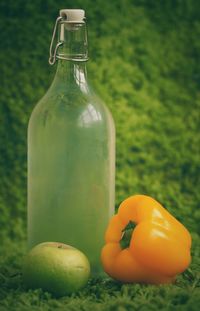 Close-up of glass bottle with yellow bell pepper and green apple on grass
