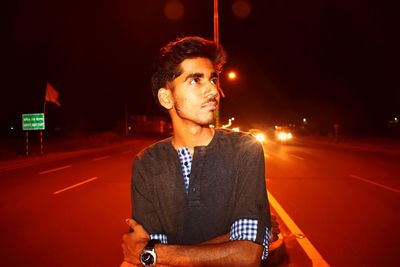 Thoughtful young man looking away while standing on road at night