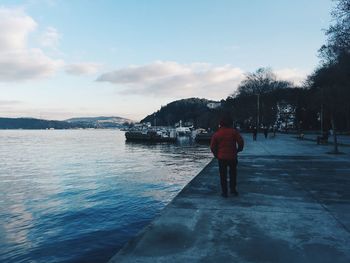 Rear view of woman walking on wet shore against sky