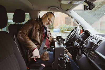 Senior man with disability fastening seat belt while sitting inside van