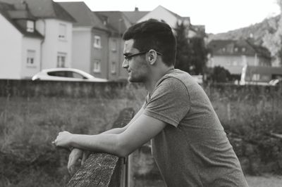 Side view of young man standing by wooden railing in city