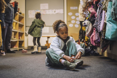 Girl wearing shoe while sitting on carpet in kindergarten