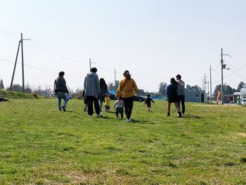 People walking on field against clear sky