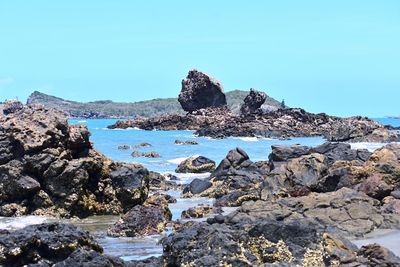 Rocks by sea against clear blue sky