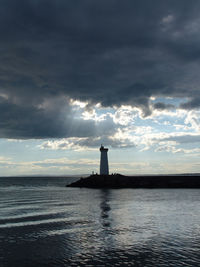 Lighthouse by sea against sky during sunset