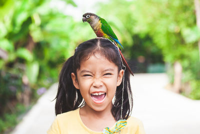 Bird perching on cheerful girl head against trees