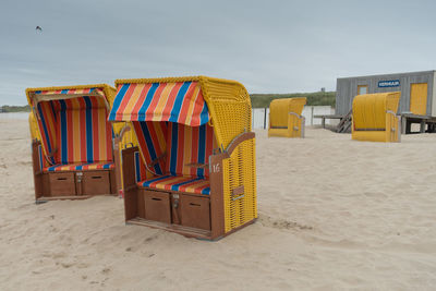 Hooded chairs on beach against sky