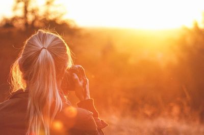 Rear view of woman photographing field at sunset