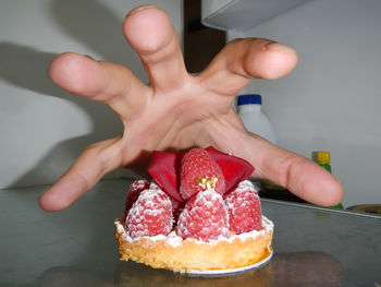 Close-up of hand reaching for fresh raspberry cake in refrigerator