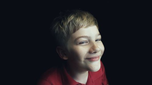 Close-up portrait of smiling boy against black background
