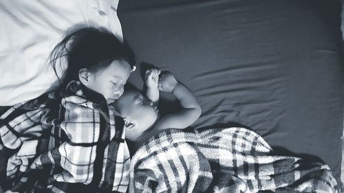 High angle view of siblings sleeping on bed at home