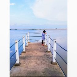 Girl standing by railing against sea and sky