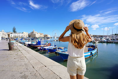 Back view of beautiful traveler girl enjoying view of trani historic town and seaport. 