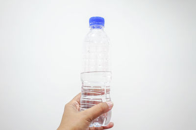 Close-up of hand holding glass bottle against white background