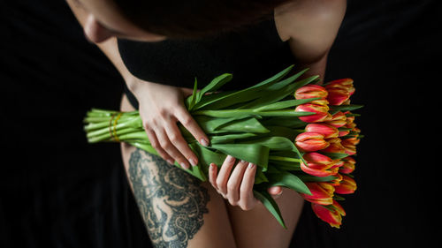 High angle view of young woman holding tulips over black background