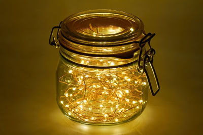 Close-up of illuminated lights in jar against yellow background