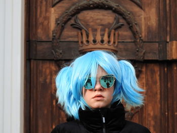 Portrait of girl with dyed hair wearing sunglasses against door