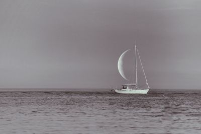 Optical illusion of sailboat sailing on sea against half moon