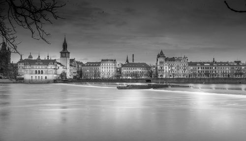 View of illuminated buildings by river against sky in city