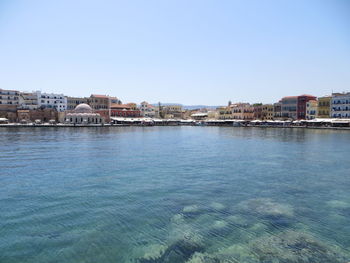 Buildings by sea against clear blue sky