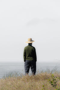 Rear view of woman wearing hat standing on field against clear sky