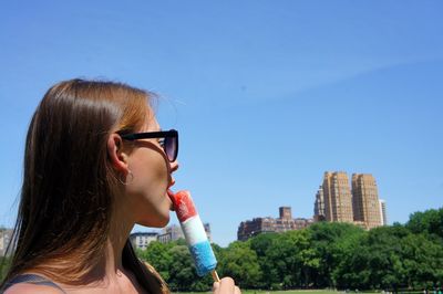 Young woman eating flavored ice in city during sunny day