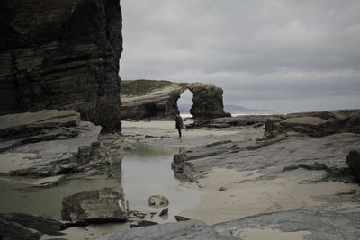 People standing on rock formation against sky