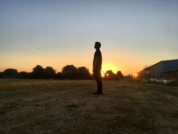 Side view of man standing on land against sky during sunset