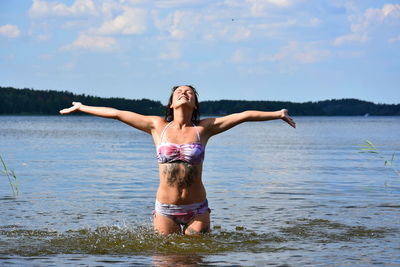 Woman with arms outstretched in lake against sky