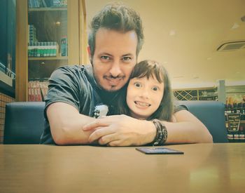 Portrait of smiling father embracing cute daughter while sitting in restaurant