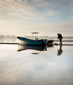 Man on boat moored at shore against sky during sunset