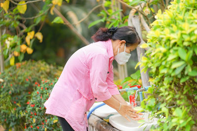 Side view of woman standing by pink flowering plants