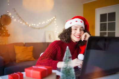 Smiling girl wearing santa hat using laptop at home