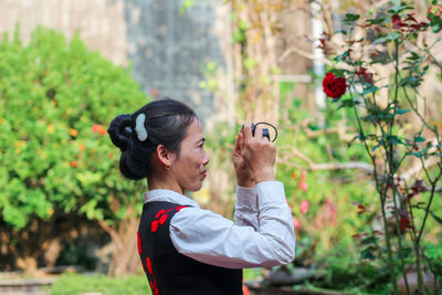 Vietnamese mid-age woman taking pictures with a small camera in the garden