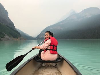 Young woman sitting on boat in lake against mountains