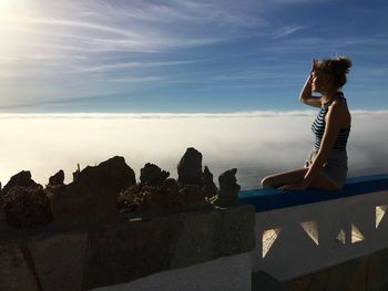 Woman sitting on retaining wall against sky