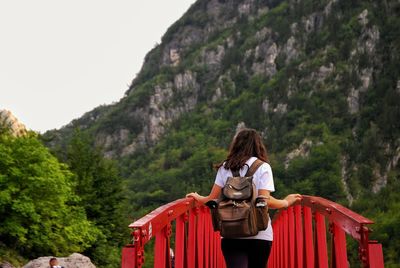 Rear view of woman standing amidst red railings against mountains