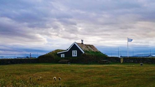 House on grassy field against cloudy sky